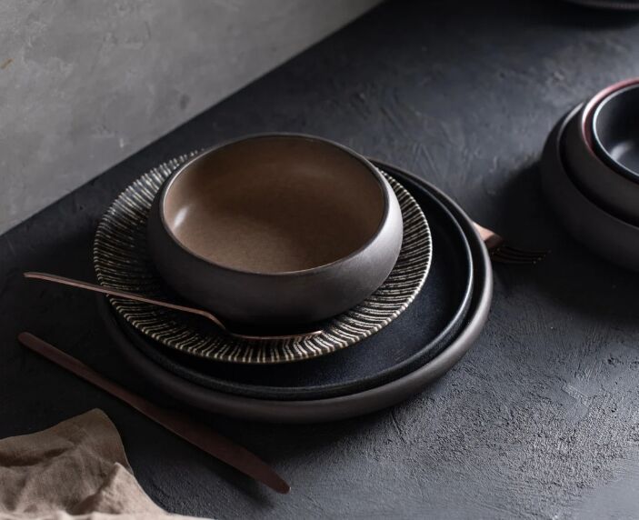 Stacked ceramic bowls and plates with textured patterns on a dark surface, creating a moody, minimalist setting. No text visible.