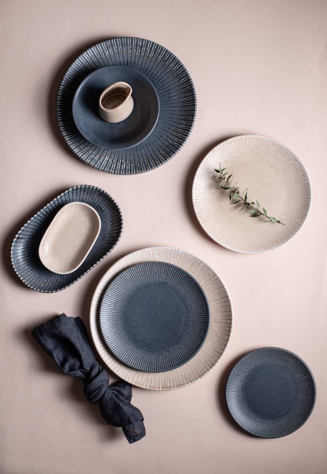 Elegant ceramic plates in blue and beige on a soft pink background, with a sprig of greenery and a dark napkin. Minimalist style.