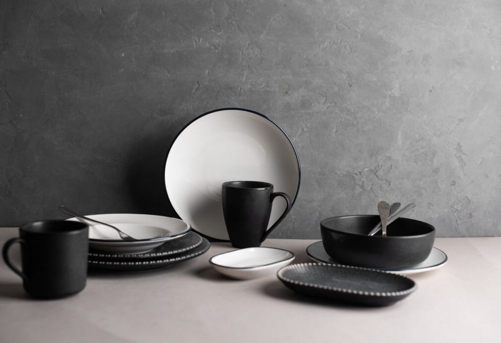Black and white ceramic dishes and mugs on a gray textured background. Simple, elegant setting with a minimalistic mood.