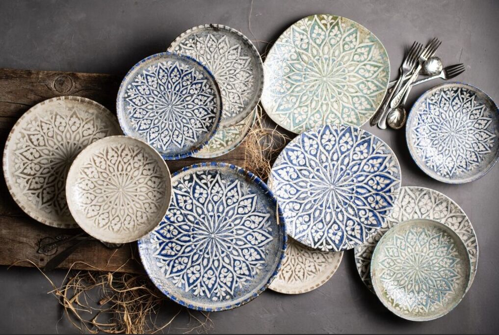 Ceramic plates with intricate blue and green patterns on a wooden surface. Forks and spoons are beside, creating a rustic vibe.