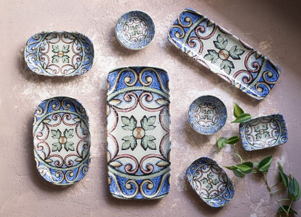 Ceramic plates and bowls with floral patterns in blue and green on a textured surface, accented by green leaves.