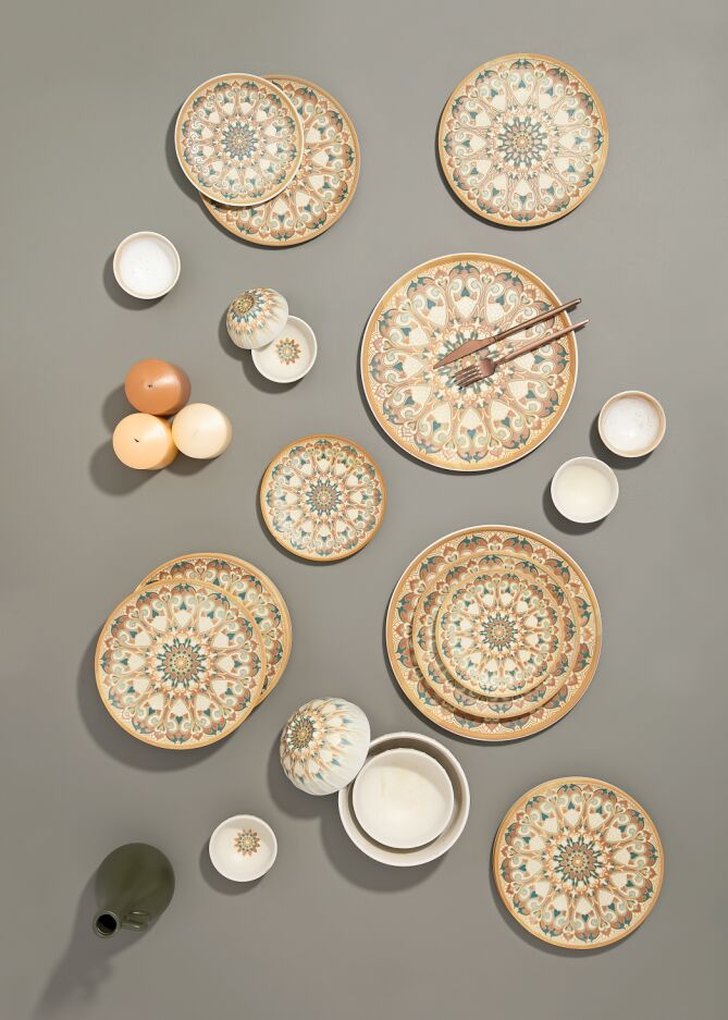 Decorative plates with intricate patterns, bowls, and candles are arranged on a gray background. A pair of chopsticks rests on one plate.